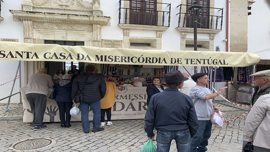 A nossa instituição voltou a marcar presença na tradicional Feira Anual do Dia de Todos os Santos com a realização da já habitual Quermesse, um momento que reúne a comunidade em torno da solidariedade.
                      <br><br>
                      Ao longo do ano, vamos reunindo diversos artigos decorativos e objetos úteis, gentilmente oferecidos por benfeitores. Muitos desses itens provêm de espólios de casas desativadas após o falecimento dos seus residentes, cujas famílias optam por doar alguns bens à instituição. Estes objetos são cuidadosamente selecionados e preparados para integrar a Quermesse.
                      <br><br>
                      Durante o dia da Feira, para além da venda destes artigos, disponibilizamos também produtos tradicionais confecionados na nossa cozinha, como broa de milho, arroz doce, broa doce e biscoitos, muito apreciados pelos visitantes.
                      <br><br>
                      O valor angariado reverte integralmente para o bem-estar dos nossos idosos, permitindo a aquisição de material lúdico e o apoio a atividades recreativas, como passeios à praia, a Fátima ou a outros destinos. Estas iniciativas são especialmente importantes para os utentes que não dispõem de retaguarda familiar, garantindo-lhes momentos de convívio, lazer e qualidade de vida.